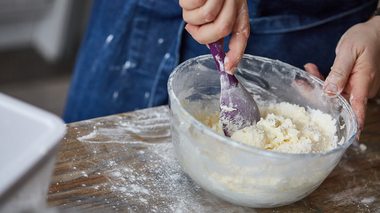 An illustrative image showing an individual mixing a cake batter in a bowl with a spoon.