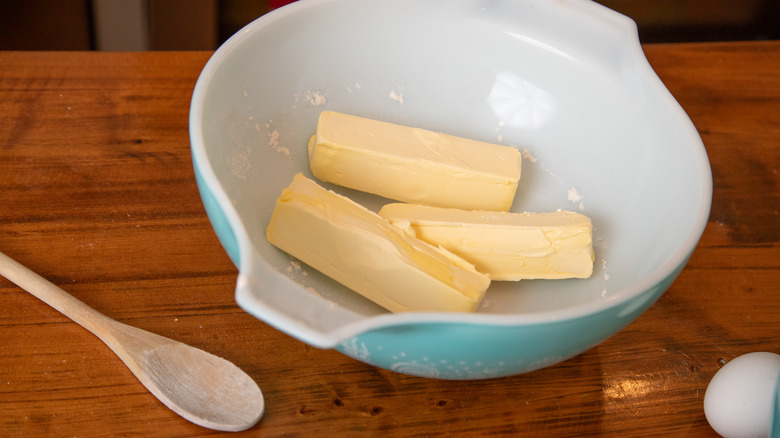 An illustrative image showing sticks of butter in a mixing bowl with a spoon on the side.