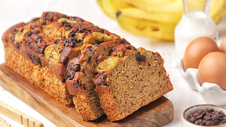 A loaf of banana bread is pictured with eggs, milk, bananas, and chocolate chips in the frame.