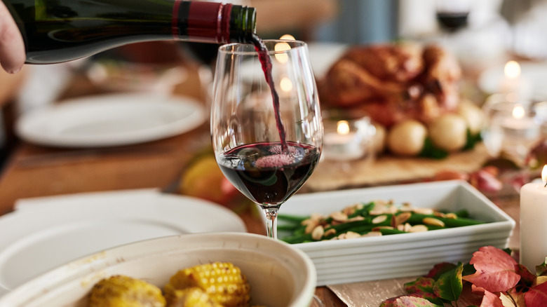 Hand pouring red wine into glass at dinner table