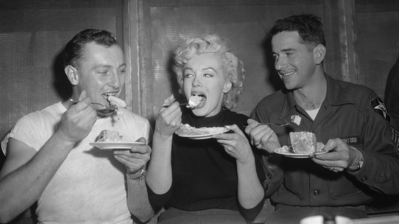 Black and white photo of Marilyn Monroe eating with two soldiers