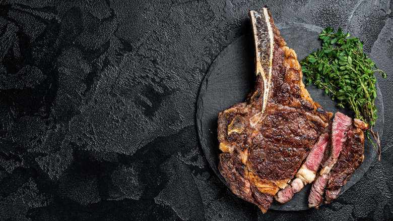 A cowboy steak has been cooked and plated with greens.