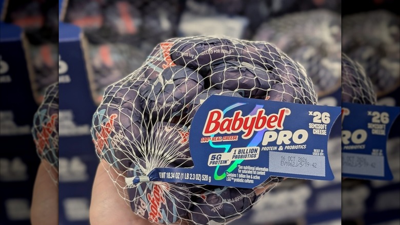 Person's hand holding many Babybel Pro Snacking Cheeses in a white netting