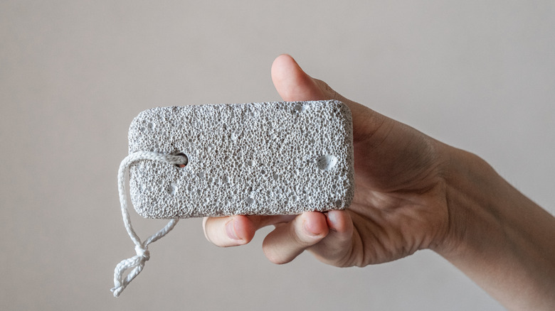 A hand holding a pumice stone against a light gray background.