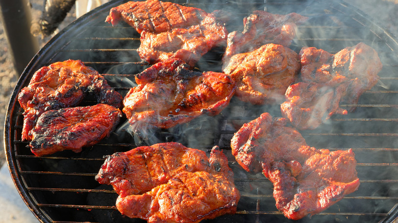 A smoky grill with a batch of juicy pork chops on top.