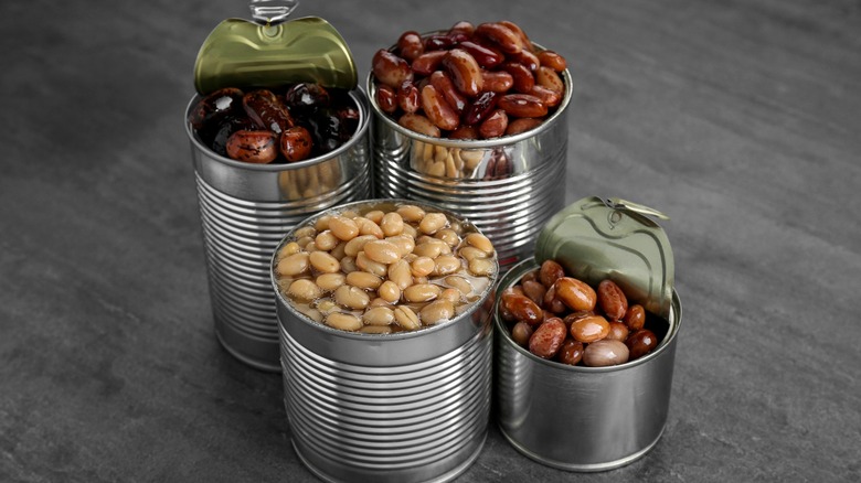 Assorted canned beans with lids popped open.