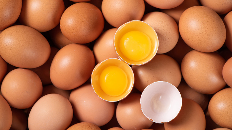Pile of brown eggs with two cracked eggs in the center.