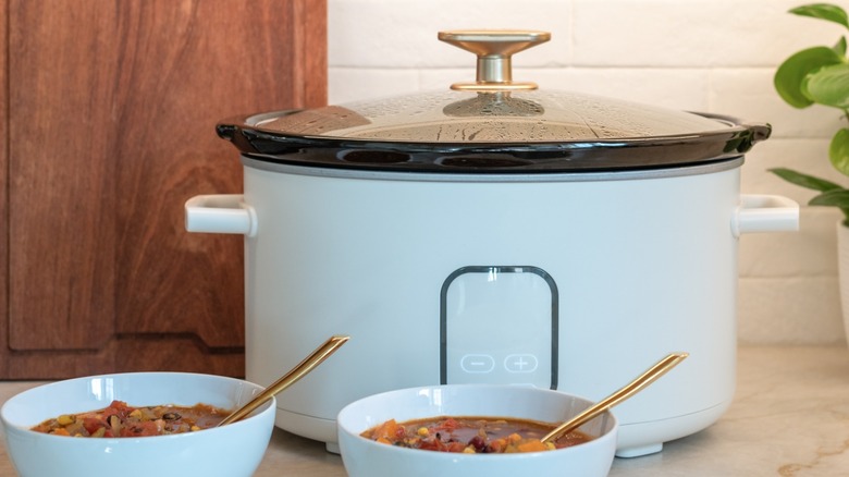 slow cooker on a counter with bowls of stew