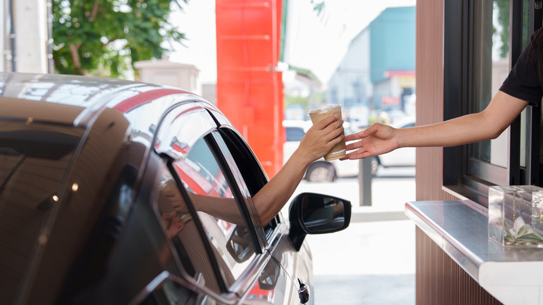 Person handing coffee to a customer at a drive-thru window.