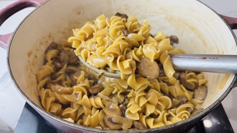 Spoon removing noodles and mushrooms from pot