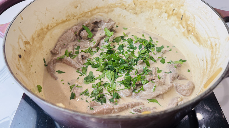 Beef stroganoff sauce, steak strips, and parsley in Dutch oven