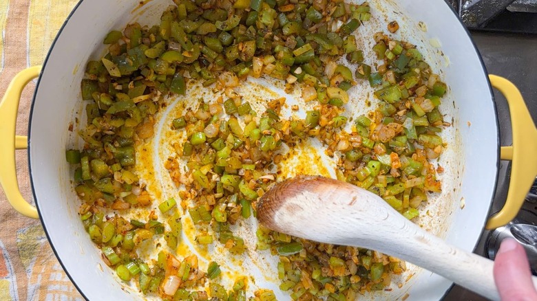 Stirring chopped aromatic vegetables and spices with wooden spoon in yellow pot on stovetop