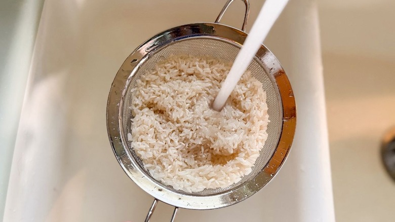 Rinsing long-grain rice in mesh strainer with water over sink