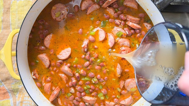 Adding chicken stock to one-pot red beans and rice with sausage in pot on stovetop