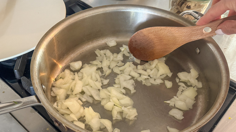 hand stirring onion in pan