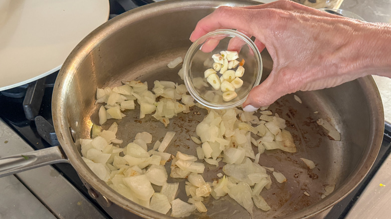 hand adding garlic to pan