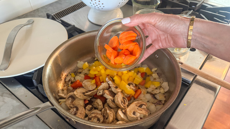 hand adding carrots to pan