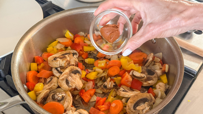 hand adding curry paste to pan