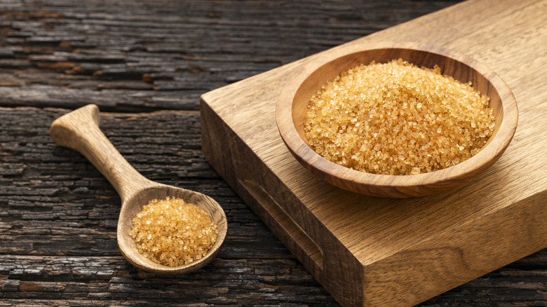 A wooden bowl of organic brown sugar with a wooden spoon full of brown sugar next to it