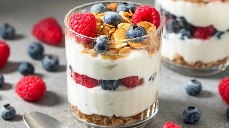 Yogurt parfait in a clear ribbed glass with fresh raspberries, blueberries, and almond granola