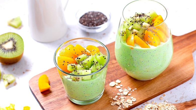 Matcha-infused chia pudding in two clear glasses topped with diced mango, kiwi, and chia seeds