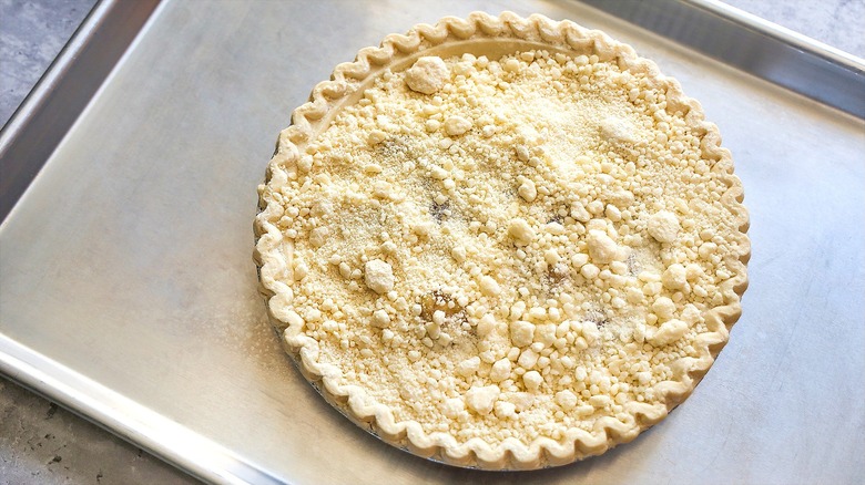 Unbaked, pre-made pie with crumble topping on metal baking sheet