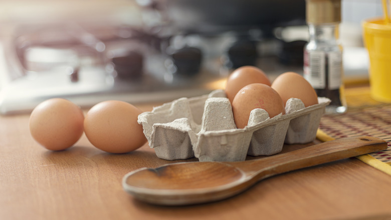 Carton of a half dozen eggs on the counter next to a wooden spoon