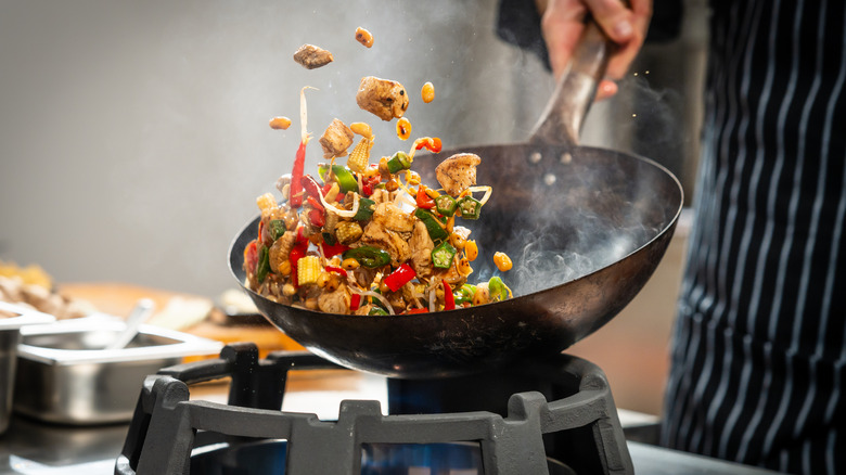 chef tossing vegetables and meat in the air while stir frying in a wok in a professional kitchen.