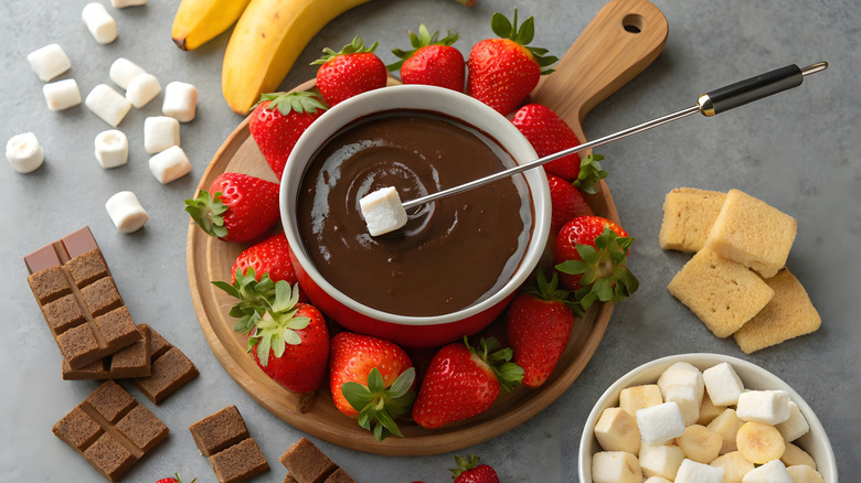 A dark chocolate fondue surrounded by dippers like fruit and marshmallows.
