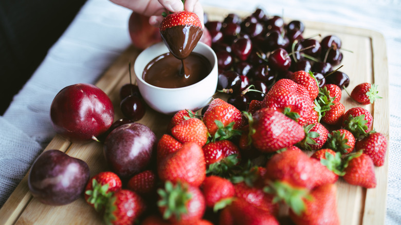 A platter of fruit and a bowl of chocolate with a strawberry being dipped in the chocolate.