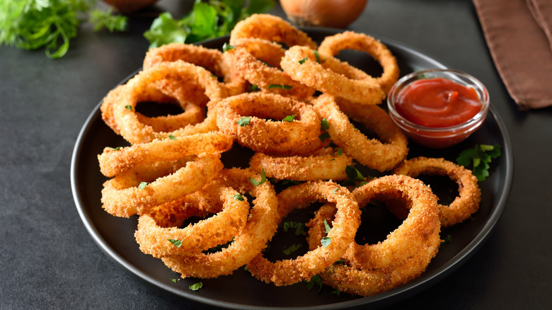 A plate filled with fried onion rings and a cup of dipping sauce
