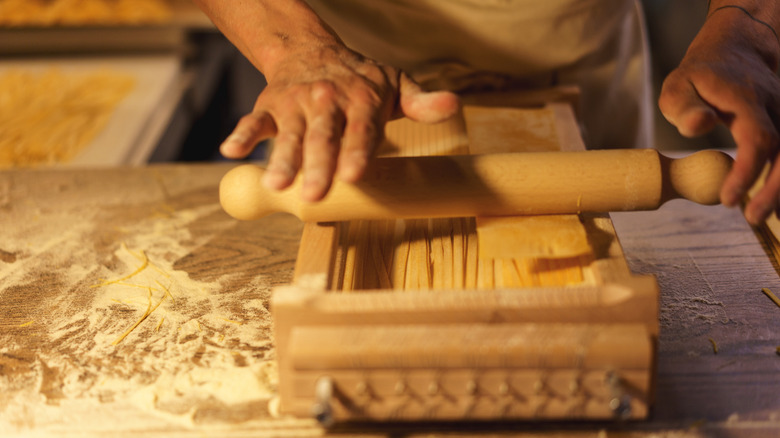 Person making chitarra pasta on a wooden frame with strings