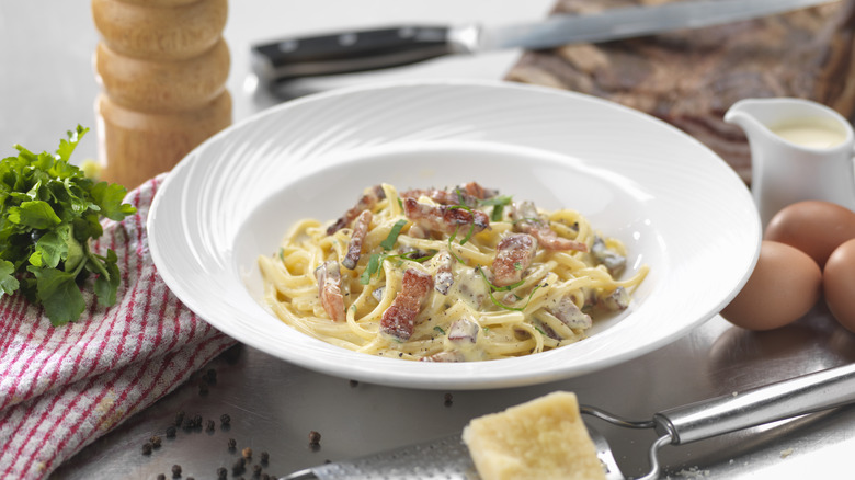 A while bowl of carbonara surrounded by the pasta's ingredients