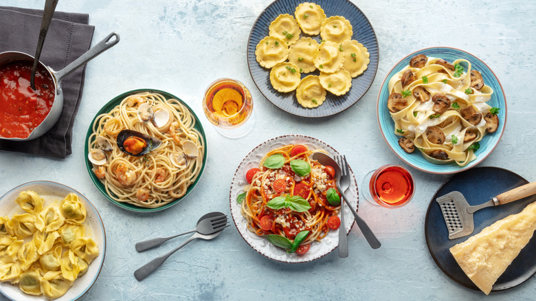 Overhead angle of different types of pasta, including seafood spaghetti and fettuccine with mushrooms, and a glass of wine