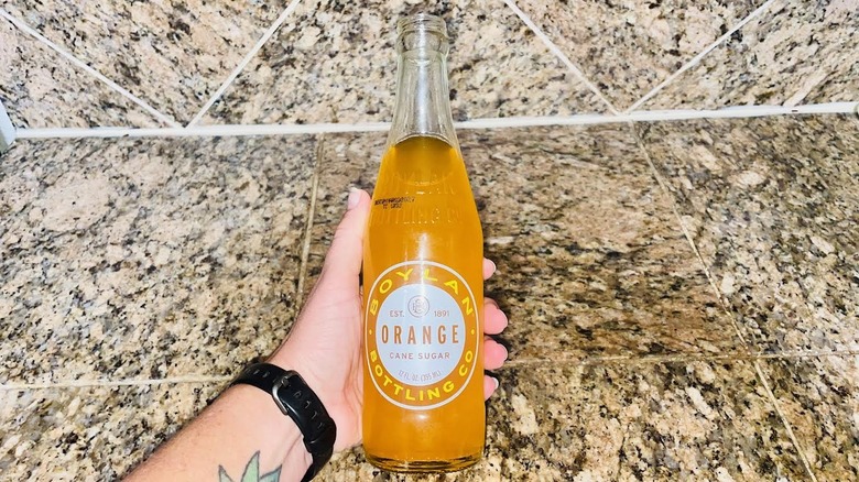 Hand holding glass bottle of Boylan Orange Soda over marble counter