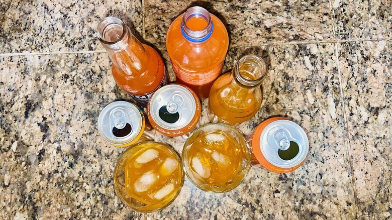 Overhead view of orange sodas in bottles, glasses, and cans
