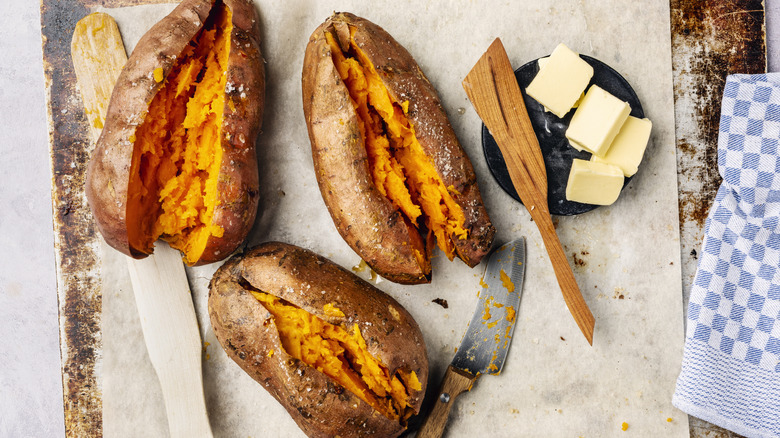 Three roasted orange sweet potatoes split down the middle with a plate of butter cubes on the side