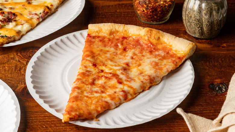 A slice of NYC pizza, made woith dough, tomato sauce, and mozzarella cheese, on a paper plate.
