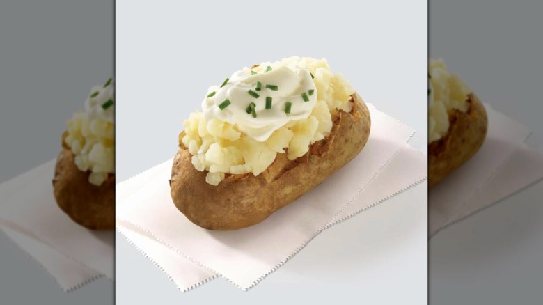 Baked potato with sour cream and chives on napkins with a white background.