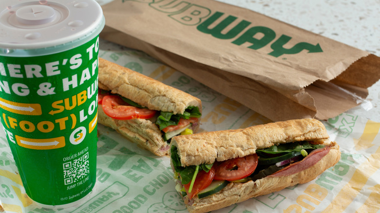 Image of Subway sandwich with wrapper and drink on a table.