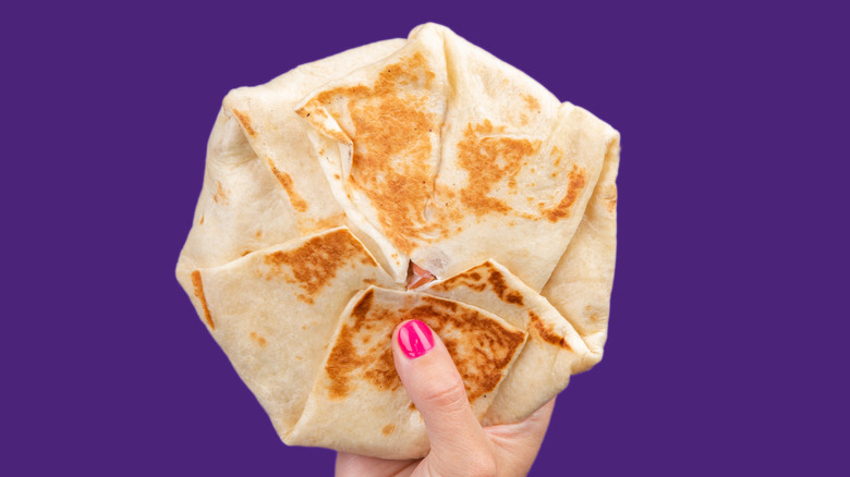 Hand holding a Taco Bell Crunchwrap Supreme.