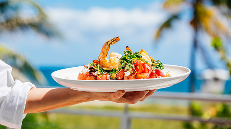 Waiter holding a plate of seafood against a tropical background