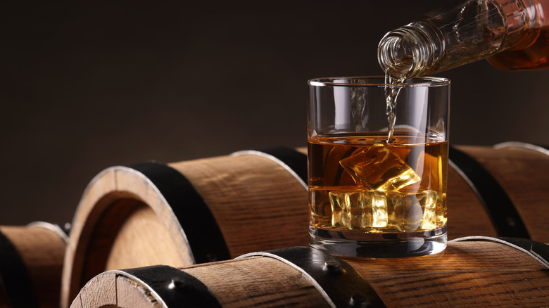 A glass of whiskey atop wood barrels.