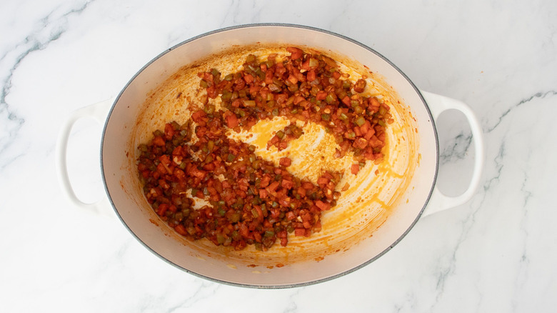 Softened diced vegetables coated in tomato paste in Dutch oven