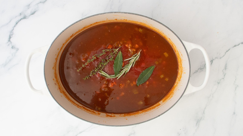 Various herbs sitting atop pomodoro sauce in Dutch oven