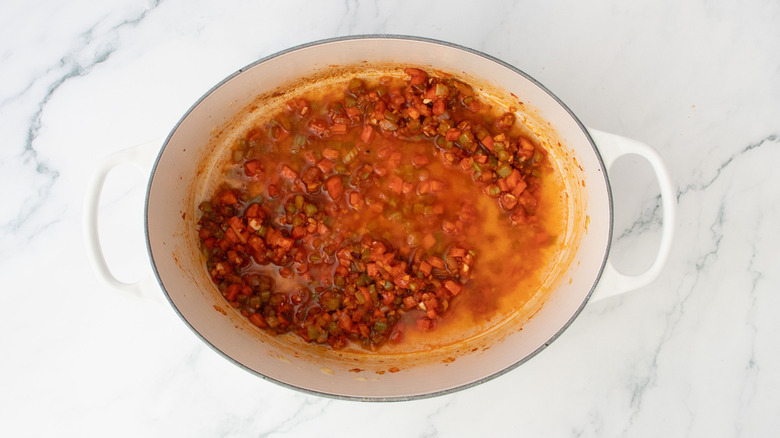 Diced vegetables coated in tomato paste with liquid in Dutch oven