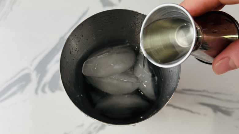 hand pouring liquor into cocktail shaker filled with ice