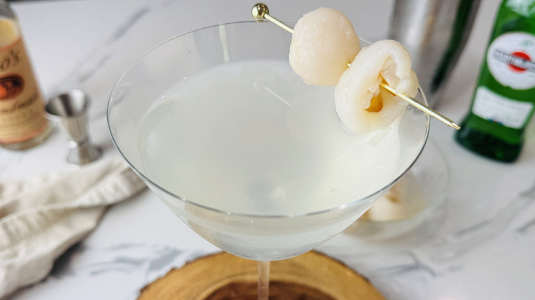 lychee martini in glass with lychee garnish and bottles behind