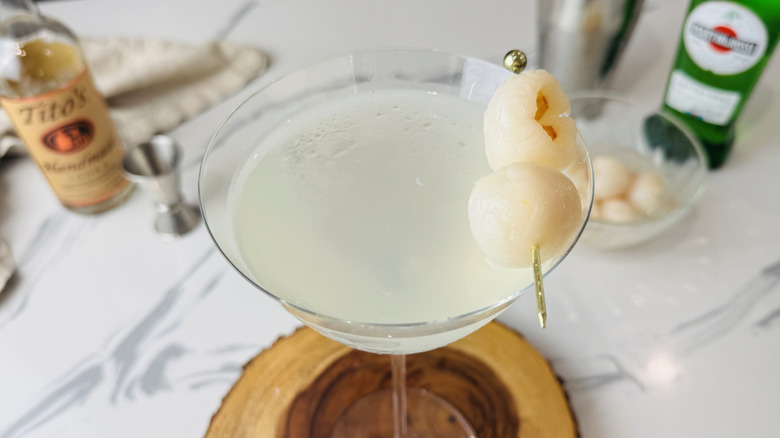 closeup of lychee martini in glass with lychee garnish on tree trunk serving board