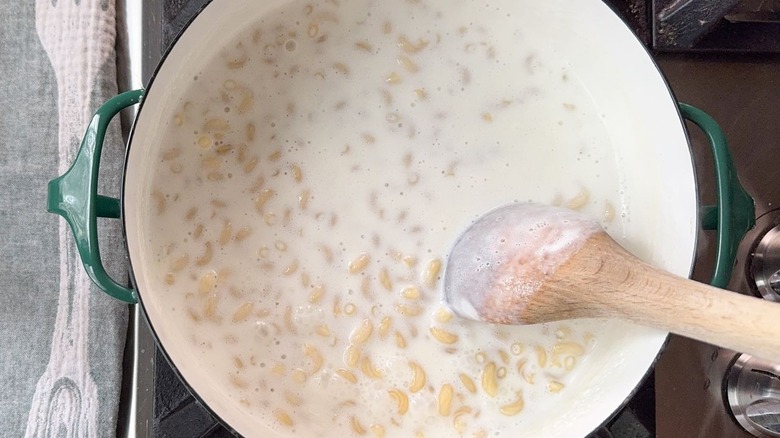 Stirring milk and macaroni noodles in large pot with wooden spoon on stovetop